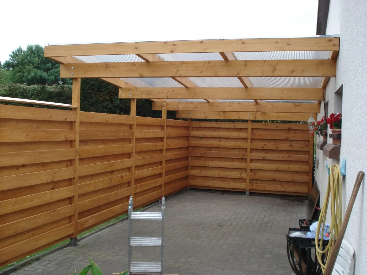 Holz Carport mit verblankten Seitenelementen und als Dach eine Holzkonstruktion auf dem Milchglas verbaut ist