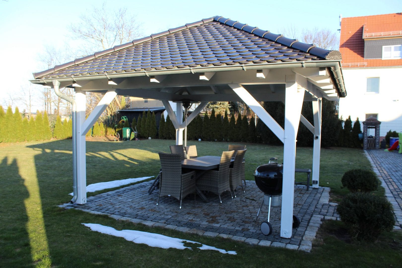 Schöne Ansicht eines viereckigen Gartenpavillons mit Zeltdach und Biberdeckung. Dachneigung beträgt ca. 30 Grad. Die umlaufende Rinne wird über nur ein Fallrohr entwässert.